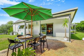 Eine Terrasse mit Tisch und Stühlen, einem grünen Sonnenschirm und einem Haus im Hintergrund.