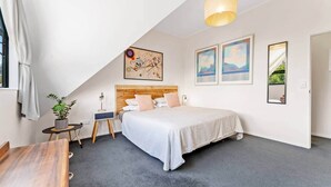A bedroom with a bed, a bedside table, a lamp, a plant, and artwork on the walls.