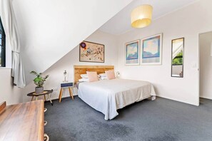 Ein Schlafzimmer mit einem Bett, einem Nachttisch, einer Lampe, einer Pflanze und Bildern an den Wänden.