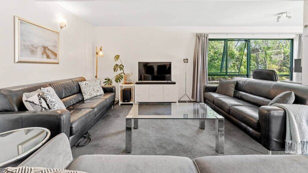 A modern living room with a sofa set, a coffee table, a TV, and a large window with curtains.