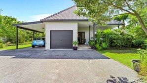A modern house with a garage, a covered driveway, and lush greenery.