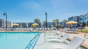 Uma piscina com espreguiçadeiras e guarda-sóis, cercada por edifícios.