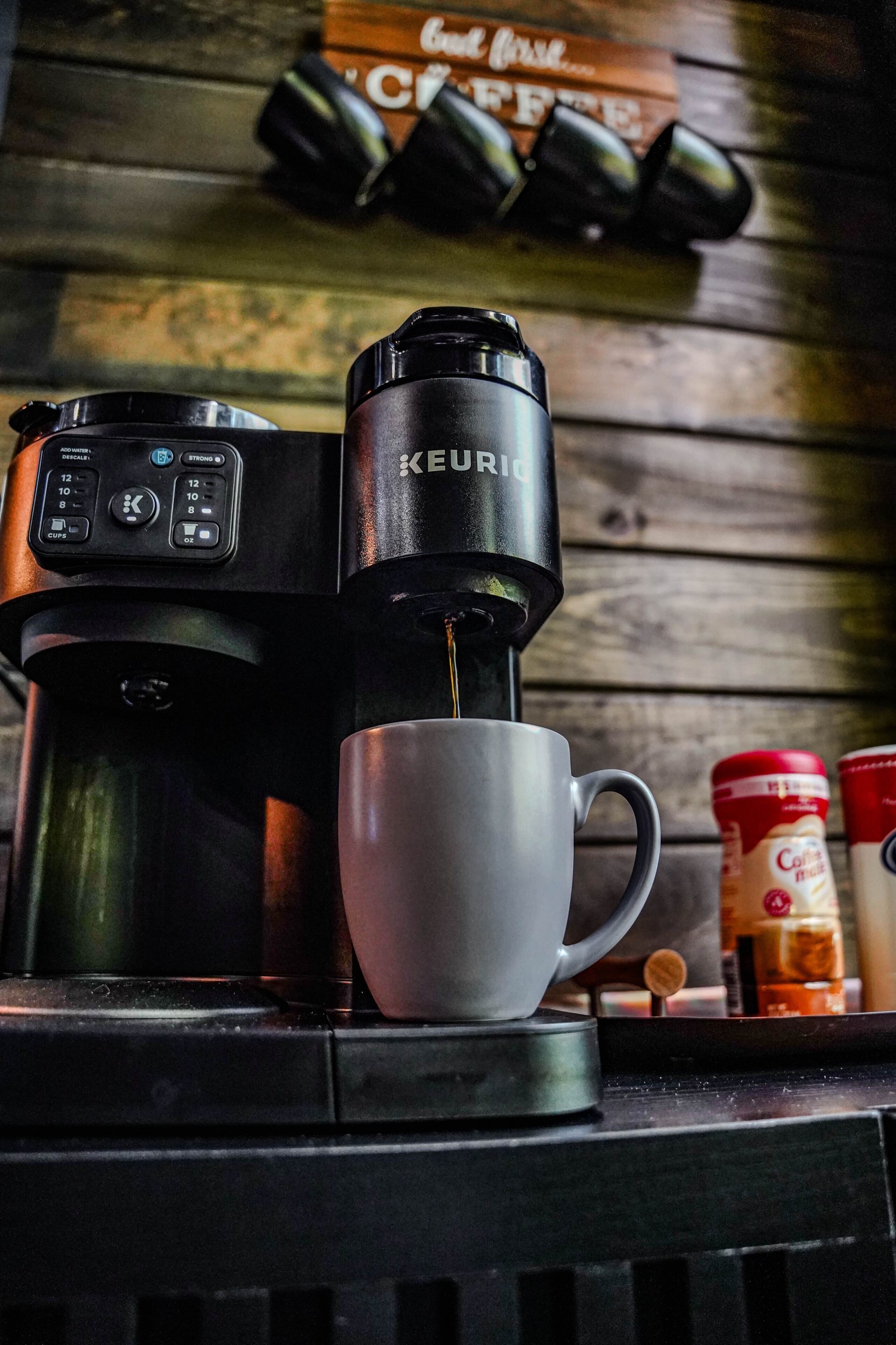 A coffee machine with a cup of coffee, a coffee grinder, and a coffee jar on a wooden surface.