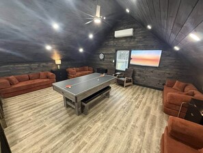 Et rum med et ping pong bord, sofaer, et ur og et billede på væggen.
