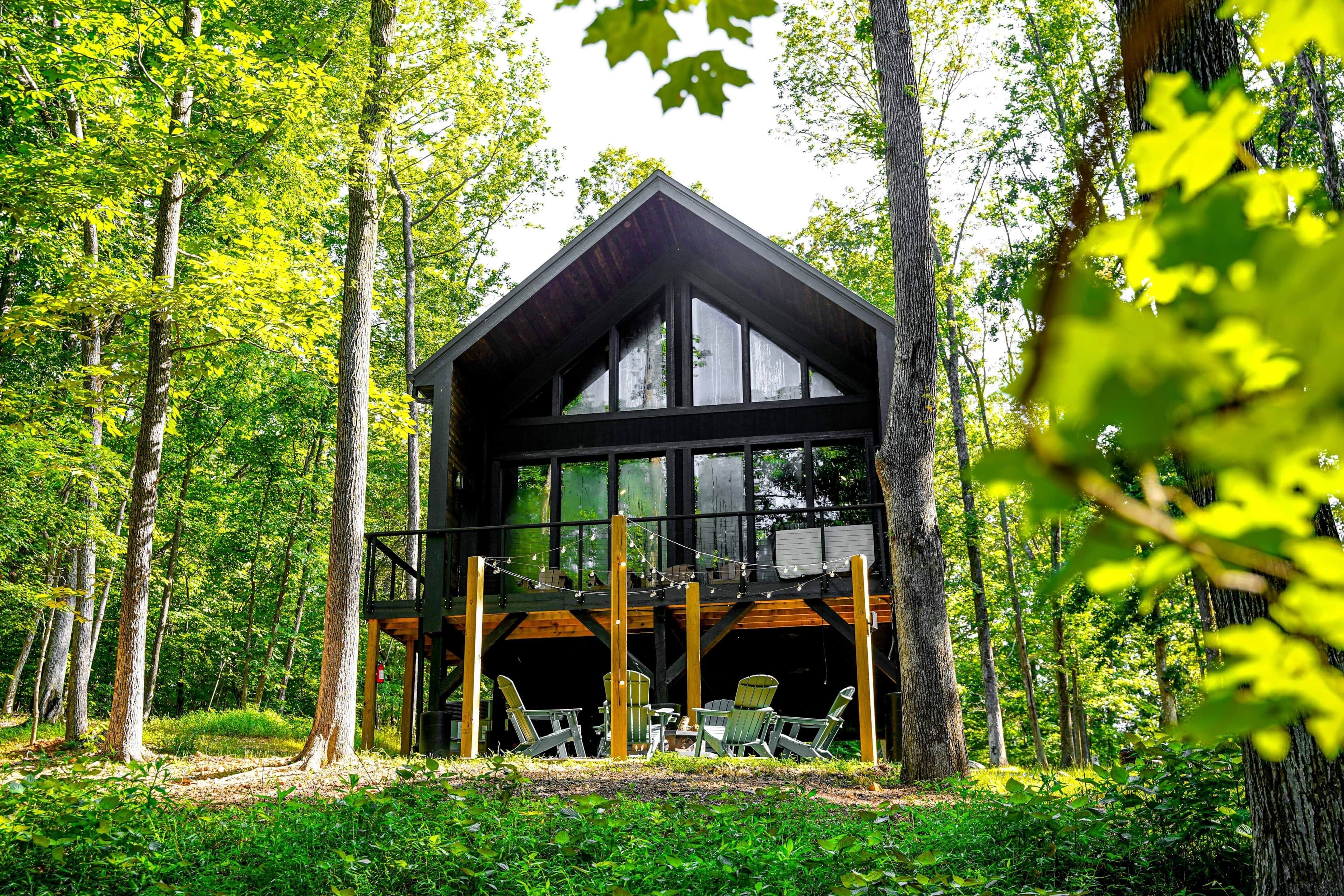 A cabin with a wooden deck, large windows, and a view of the forest.