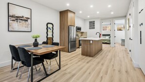 A modern kitchen with a central island, a dining area with a table and chairs, and a living space with a sofa and a TV. - Modern, spacious 2BR suite in Calgary, 13 min to downtown, private entrance (Calgary)