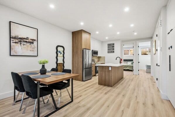 A modern kitchen with a central island, a dining area with a table and chairs, and a living space with a sofa and a TV.
