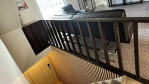 Uma escada com corrimão preto leva a uma sala de estar com sofá e televisão.
