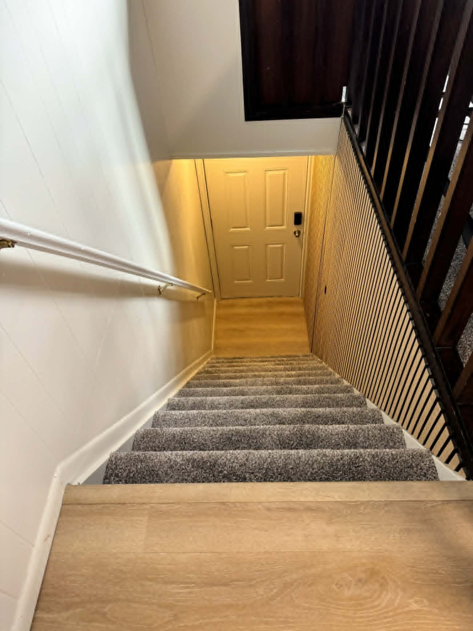 A staircase with a wooden handrail, carpeted steps, and a door at the top.