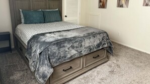 Quarto com cama, penteadeira, porta e três quadros pendurados na parede.