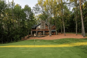 A lodge with a stone facade, wooden deck, and a flag on the green.