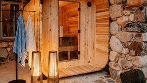 Una sauna de madera con pared de piedra, puerta de cristal y dos lámparas de pie.