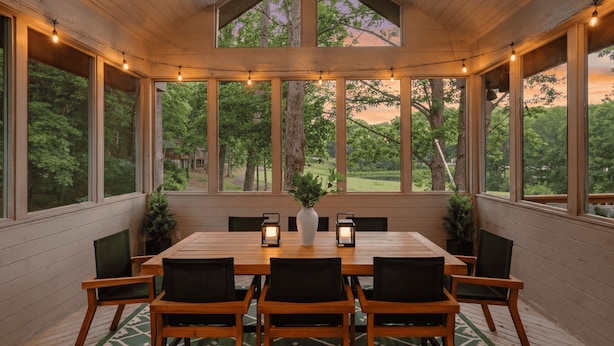 Un área de comedor techada con una mesa y sillas de madera, ventanas grandes y luces colgantes.