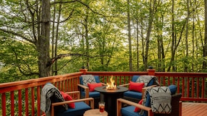 Una terraza con mobiliario de mimbre, una chimenea y vistas a un bosque.