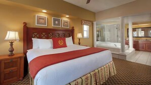 A hotel room with a large bed, two bedside lamps, a ceiling fan, a bathroom with a bathtub, and a kitchen area. - Westgate town center resort / 2 bedrooms (Kissimmee)