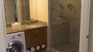 A bathroom with a washing machine, a sink, a mirror, and a glass-enclosed shower. - Westgate town center resort / 2 bedrooms (Kissimmee)
