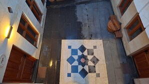 A courtyard with a tiled floor, potted plants, and wooden doors. - Ela Sultan Han (Gaziantep)