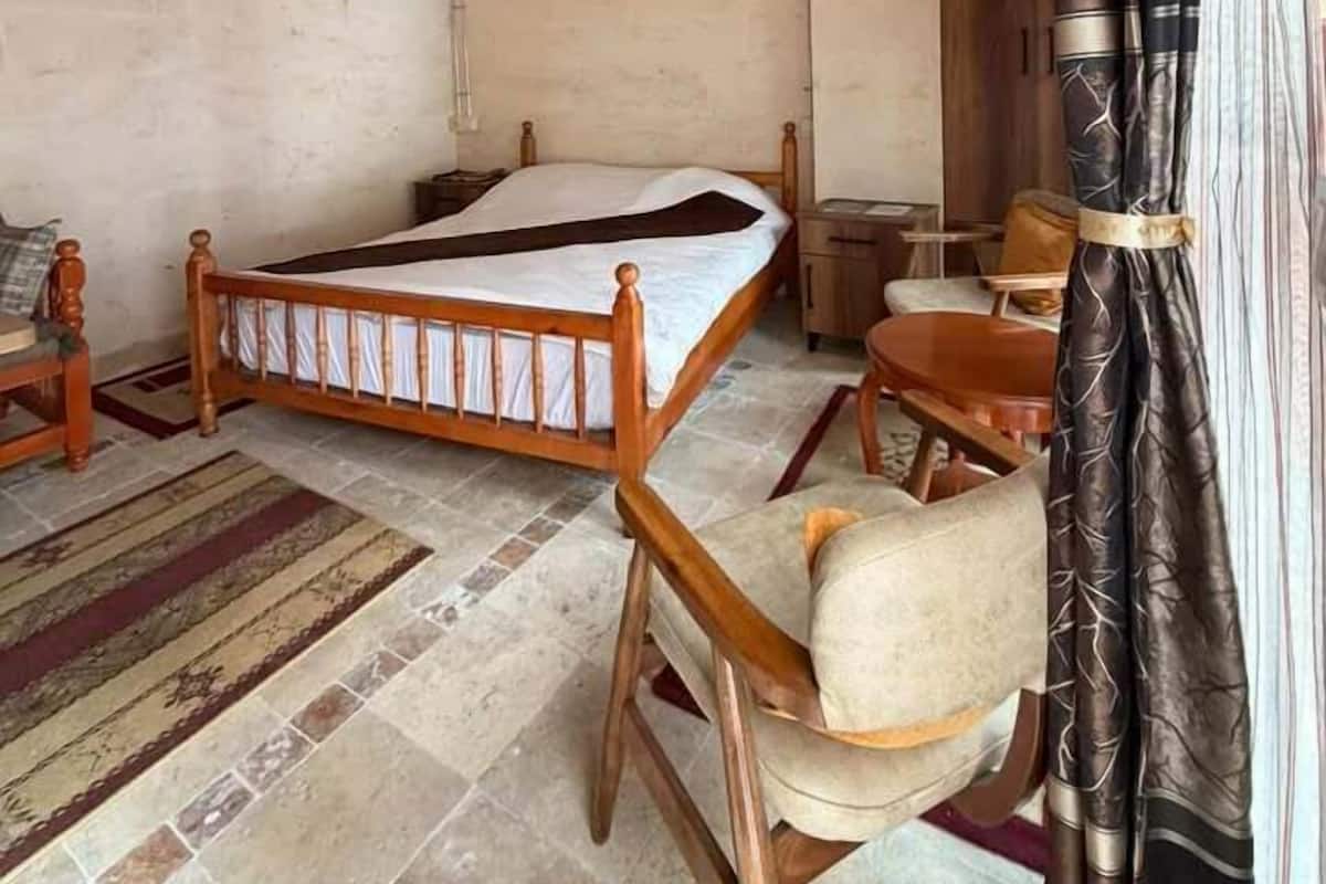 Une pièce avec un plafond en bois, un lit avec un cadre en bois, une petite table, une chaise et un rideau.