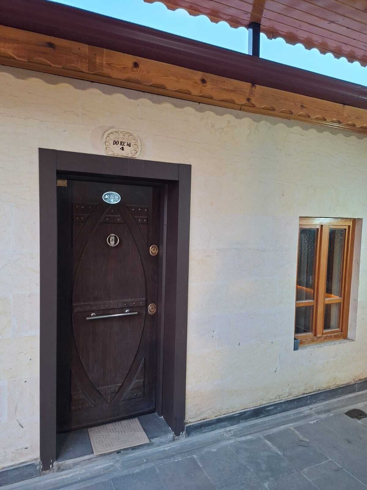 Una puerta de madera oscura con un picaporte metálico, una ventana pequeña con marcos de madera y un letrero encima de la puerta.