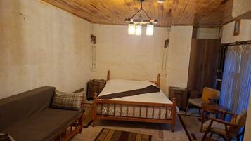 A room with a wooden ceiling, a bed with a white and black bedspread, a wooden nightstand, a wooden chair, and a small table.
