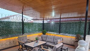 An outdoor patio with a wooden ceiling, a sofa, chairs, and a table. - Ela Sultan Han (Gaziantep)