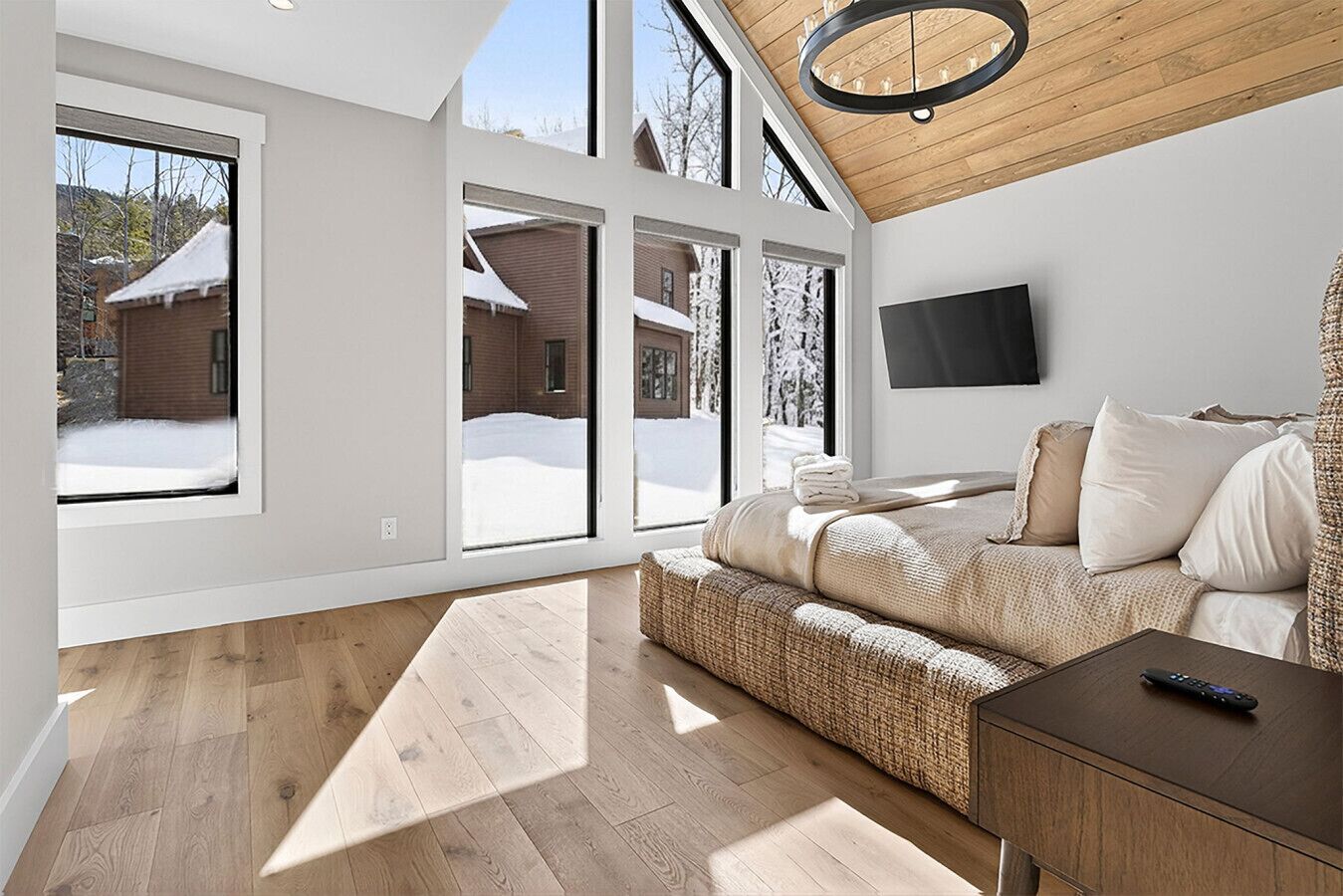 Une chambre moderne avec un grand lit, une télévision et une vue sur un paysage enneigé, visible à travers de grandes fenêtres.