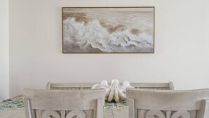 Une table à manger avec des chaises, une œuvre d’art encadrée au-dessus, et un objet décoratif posé sur la table.