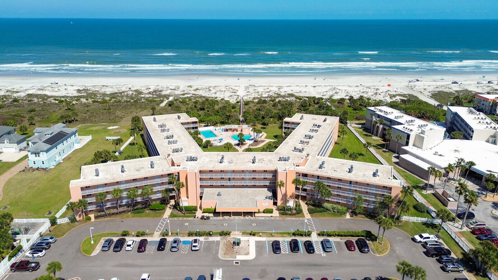 A hotel with a central courtyard, multiple parking lots, and a beach view.