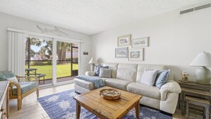 Un salon comprenant un canapé, une table basse en bois, un fauteuil en osier et une vue sur un jardin, accessible par des portes vitrées.