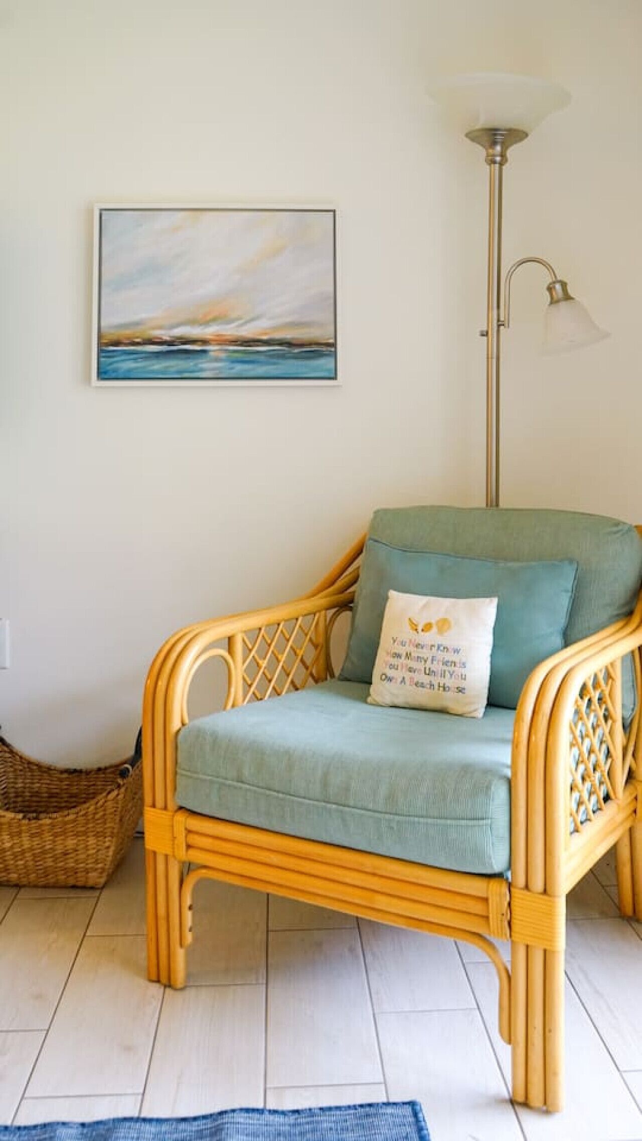 A wicker chair with a cushion, a wall-mounted painting, a floor lamp, and a wicker basket.