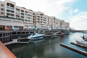 Un port de plaisance où est amarré un grand yacht, un hôtel à plusieurs étages doté de balcons, et une promenade au bord de l’eau où règne la tranquillité.