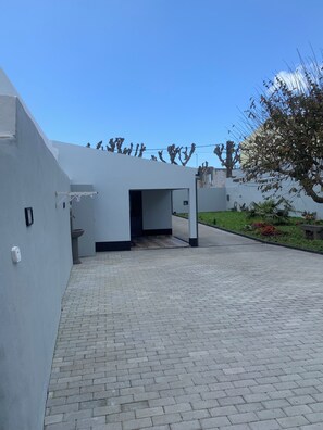 Ein modernes Gebäude mit gepflastertem Innenhof, einem gut sichtbaren Eingang und einer kleinen Grünanlage mit Pflanzen.