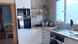 Kompakti keittiö, jossa on sisäänrakennettu uuni, mikroaaltouuni ja astianpesukone, ikkuna, josta tulee luonnonvaloa, sekä pieni työtaso.
