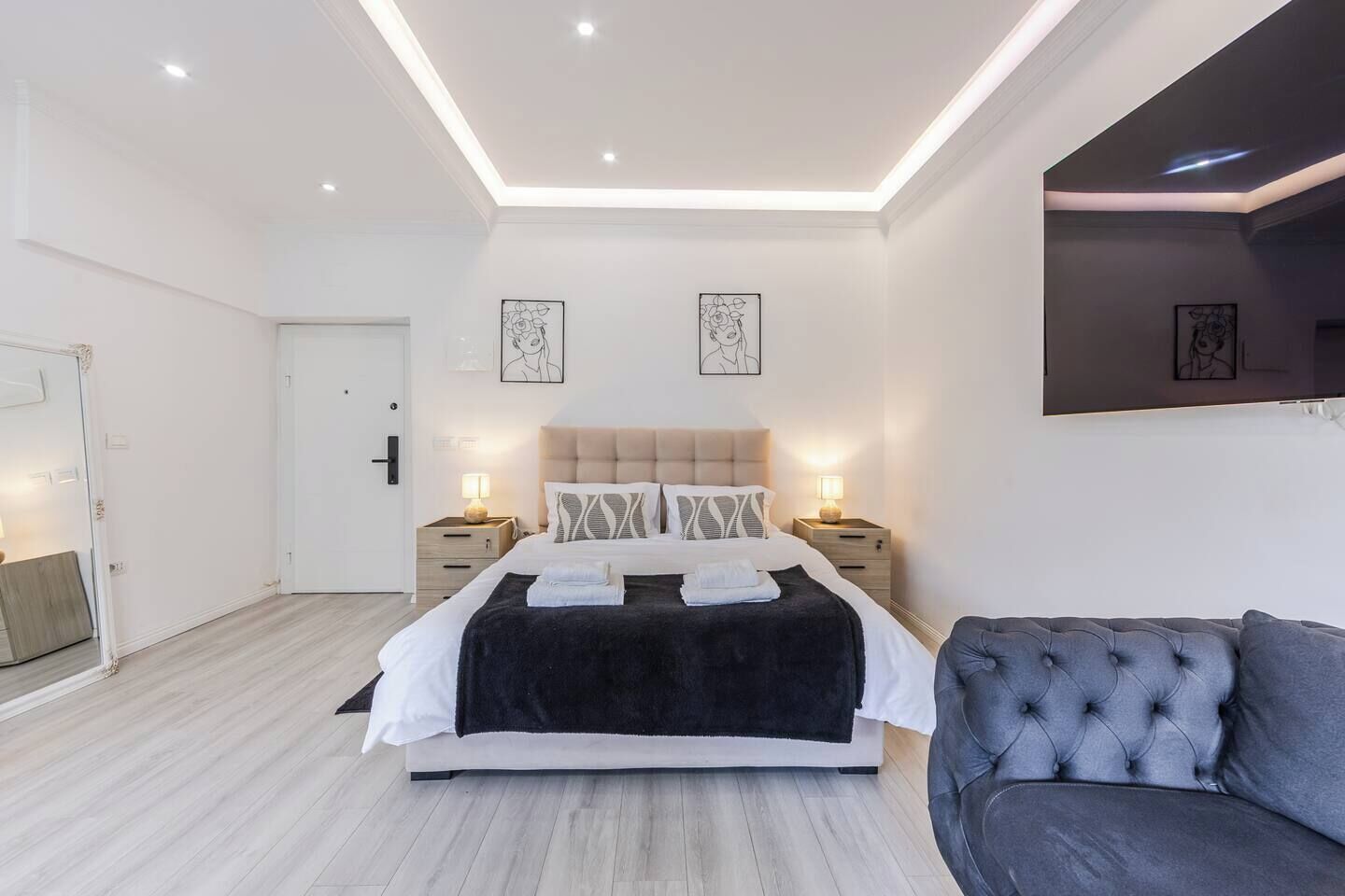 A modern bedroom with a bed, bedside tables, a sofa, and artwork on the walls.