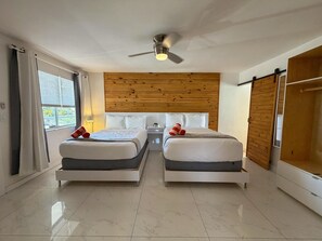 Ein Hotelzimmer mit zwei Betten, einem Deckenventilator, einem Holzkopfteil, einer Schiebetür und Blick ins Freie.