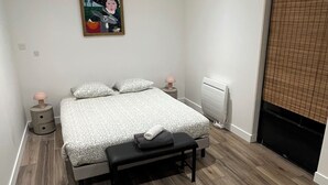 A bedroom with a bed, bedside tables, a bench, a radiator, and a painting on the wall. - Peaceful and spacious T3 in the heart of Bordeaux (Bordeaux)