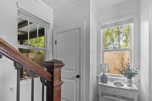 A staircase with wooden handrails, a white door, and a window with a view of trees.