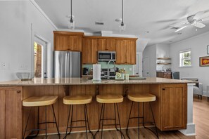 A modern kitchen with wooden cabinets, stainless steel appliances, a large island with stools, and pendant lighting.