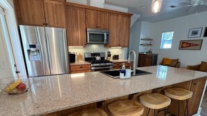 A modern kitchen with wooden cabinets, stainless steel appliances, a granite countertop, and bar stools.