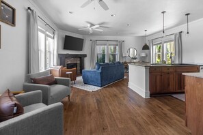 A spacious living area with a fireplace, a blue sofa, grey armchairs, and wooden flooring.