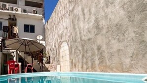 A swimming pool with a clear blue water, a building with a textured wall, and a red umbrella. - Pousada Recanto Paradise  (Ipojuca)
