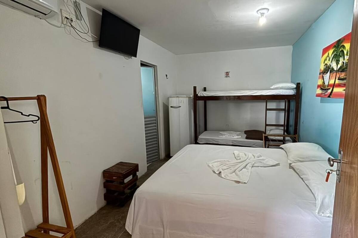 Ένα δωμάτιο με ένα διπλό κρεβάτι, μια ξύλινη ντουλάπα, μια τηλεόραση και έναν πίνακα στον τοίχο.
