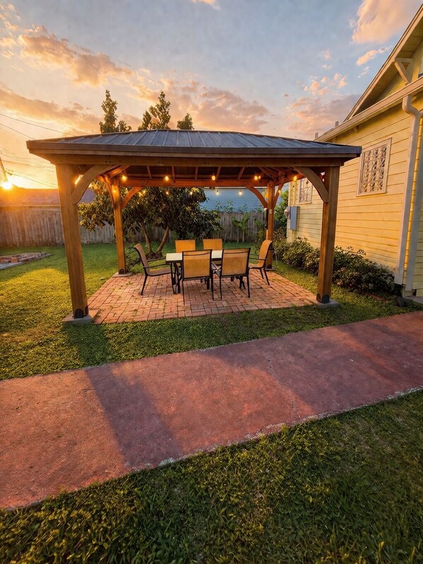 Eine überdachte Terrasse mit Backsteinboden, einer Holz-Pergola und Gartenmöbeln.