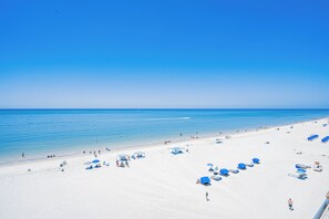 Ein Strand mit weißem Sand, klarem, blauem Wasser und mehreren blauen Sonnenschirmen.