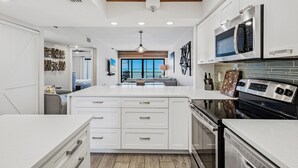 A modern kitchen with white cabinetry, a central island, stainless steel appliances, and a wooden ceiling. - 603 Villa Madeira White Sand Beachfront Condo with Stunning Sunsets (Madeira Beach)