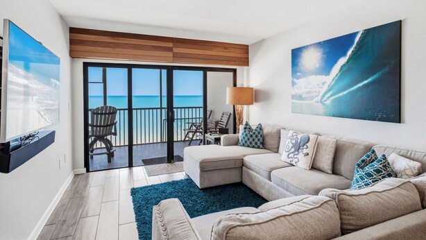 A modern living room with a large sofa, a coffee table, and a view of the ocean through a sliding glass door. - 603 Villa Madeira White Sand Beachfront Condo with Stunning Sunsets (Madeira Beach)