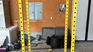 Ein Fitnessraum mit einem gelb-schwarz gestreiften Hantelgestell, einem Deckenventilator und einem Betonboden.