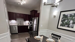 A dining area with a table set for four, a kitchen in the background, and a ceiling light fixture. - Spacious Corporate Furnished One Bedroom/One Bath in Alpharetta. (Alpharetta)
