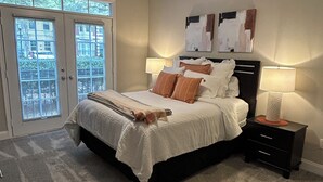 A bedroom with a bed, two bedside tables with lamps, a ceiling fan, and a view through a door. - Spacious Corporate Furnished One Bedroom/One Bath in Alpharetta. (Alpharetta)
