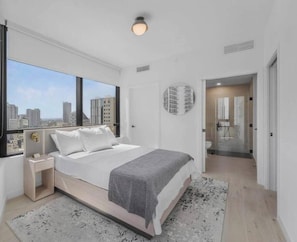A modern bedroom with a large window, a bed, a bedside table, and a circular wall decoration. - Chic 1BR in District 225 / Sleeps 4 (Miami)